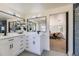 A bright bathroom features a double vanity with modern lighting, mirrors, and dark hardware and a view into the bedroom at 7208 S Xanthia Way, Centennial, CO 80112