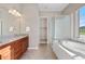 Bright bathroom featuring a soaking tub, glass shower, dual sinks, and wood cabinets at 2600 Reserve Ct, Erie, CO 80516