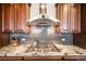 Close-up of the cooktop, featuring stainless steel range hood, granite counters, and tile backsplash at 13912 Ashgrove Cir, Parker, CO 80134