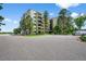View of the building featuring an asphalt parking lot, exterior landscaping, and an array of green trees at 13902 E Marina Dr # 303, Aurora, CO 80014