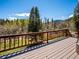 Deck view of the treeline and mountains through a wooden railing on a sunny day at 34075 Grouse Ln, Evergreen, CO 80439