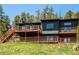 Two-story home with a large deck, wood siding, chimney, and stairs against a backdrop of trees and blue sky at 34075 Grouse Ln, Evergreen, CO 80439