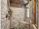 Tiled shower with a wooden framed window and a stone-like design for the walls and mosaic tile for the shower floor at 34075 Grouse Ln, Evergreen, CO 80439