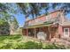 Backyard features lush green lawn, mature trees, covered patio and red brick exterior at 3825 S Peach Way, Denver, CO 80237