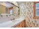 Bright bathroom featuring wallpaper, a window, a mirror and a tiled countertop with sink at 3825 S Peach Way, Denver, CO 80237