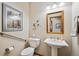 A half-bath with a cream-colored pedestal sink, wooden mirror, and picture above the toilet has updated features at 7700 W Grand Ave, Littleton, CO 80123