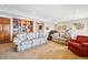 Spacious carpeted living room featuring floral couches, a wooden bookcase, and ample room for comfortable living at 7700 W Grand Ave, Littleton, CO 80123