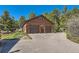 A two-car detached garage with flowers, exterior lighting, mature trees, and a paved driveway at 10450 Hondah Dr, Littleton, CO 80127