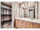 Neutral-toned bathroom featuring dual sinks, light wood cabinetry, and a shower/tub combo with decorative shower curtain at 527 Stonemont Dr, Castle Pines, CO 80108
