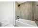 Well-lit bathroom featuring a white tub with vertically placed, gray ceramic tiling and a modern toilet at 8701 E Briarwood Blvd, Centennial, CO 80112