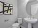 Modern powder room featuring an oval mirror, pedestal sink, and stylish black and gold abstract art at 5399 Valentia St, Denver, CO 80238