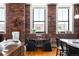 Open-concept loft dining area features exposed brick wall, hardwood flooring, and plentiful natural light from large windows at 2261 Blake St # 2G, Denver, CO 80205