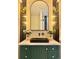 Elegant bathroom vanity with a black sink, arched mirror, sconces, and green cabinetry at 5563 E Jefferson Ave, Denver, CO 80237