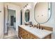 Charming bathroom featuring double sinks, oval mirrors, wood vanity and a doorway leading to an adjacent bedroom at 18330 Archers Dr, Monument, CO 80132