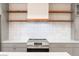 Close up of modern stainless steel oven and stove, with open wood shelving above the white backsplash at 1048 Knox Ct, Denver, CO 80204