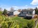 Wide shot of the backyard showing the deck off of the home, surrounded by green lawn and fencing at 10895 W Bowles Pl, Littleton, CO 80127