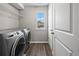 Bright laundry room featuring modern washer and dryer, window, shelving, and wood-look floors at 9716 Uravan St, Commerce City, CO 80022