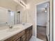 Bathroom vanity featuring double sinks and wood drawers with updated lighting and a view into the bedroom at 12953 Bridge View Ln, Parker, CO 80134