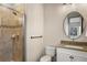 Cozy bathroom with a glass-enclosed shower, neutral tile, round mirror and single sink vanity at 15252 W Warren Dr, Lakewood, CO 80228