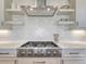 Close-up of the gas stovetop and range hood, with white cabinets, white countertops, and textured backsplash at 2690 Fox View Trl, Franktown, CO 80116