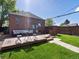 Backyard featuring a wooden deck with outdoor seating, a lush lawn, and a charming brick house under a clear blue sky at 3401 N Steele St, Denver, CO 80205