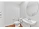 Clean half bathroom featuring a pedestal sink, a round mirror, and white walls at 8943 Tappy Toorie Cir, Highlands Ranch, CO 80129