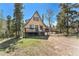A-frame cabin with a deck surrounded by lush greenery and tall trees, set against a clear blue sky at 9185 Jill Dr, Conifer, CO 80433
