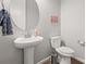 Bathroom featuring a pedestal sink, round mirror, toilet, and modern fixtures at 7268 Greenwater Cir, Castle Rock, CO 80108