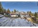 Exterior view of a blue home with a garage and driveway, set against a snowy, wooded backdrop at 27732 Squaw Pass Rd, Evergreen, CO 80439