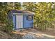 Blue shed on a sunny lot, featuring a white door and trim, surrounded by forest and landscaping at 27732 Squaw Pass Rd, Evergreen, CO 80439