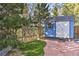 Charming blue shed with white trim, nestled in a yard with gravel and a backdrop of tall trees at 27732 Squaw Pass Rd, Evergreen, CO 80439