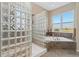 Bright bathroom featuring glass block shower, soaking tub, and scenic views at 881 Kirby Ct, Watkins, CO 80137