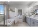 Bright bathroom featuring a large tub, dual sink vanity with grey cabinets, and an open doorway to the main bedroom at 23252 E Glidden Dr, Aurora, CO 80016