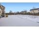 Fenced backyard with a snow covered lawn and trees on a clear, sunny day at 1945 Basil St, Strasburg, CO 80136