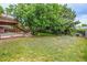 Landscaped backyard with lush lawn, mature tree, garden beds, and upper level wood deck with stairs at 9832 High St, Thornton, CO 80229
