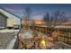 Backyard with fire pit surrounded by chairs, stone retaining wall, gravel, and fenced perimeter at twilight at 4296 Clover Ln, Brighton, CO 80601