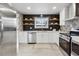 Bright kitchen featuring white cabinets, stainless steel appliances, and modern black backsplash with wood shelves at 9962 W 77Th Ave, Arvada, CO 80005