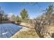 View of the backyard, featuring a lawn partially covered in snow, a wooden fence, and mature trees at 10726 Amesbury Way, Highlands Ranch, CO 80126