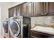 Well-equipped laundry room with front-loading machines, dark cabinets, countertop space, and modern backsplash at 6019 S Little River Way, Aurora, CO 80016