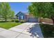 Blue and brick home featuring a lush green lawn, mature trees, and an extended concrete driveway at 2670 E 136Th Pl, Thornton, CO 80602
