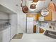 Galley kitchen featuring white appliances, light wood cabinets, and pot rack above the sink at 8621 E Dry Creek Rd # 325, Englewood, CO 80112