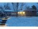 Charming home at dusk with snow-covered yard and illuminated pathway to front door at 11845 W 30Th Pl, Lakewood, CO 80215