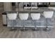 A modern kitchen island features a gray stone facade, stainless steel appliances, and sleek white bar stools at 9694 Truckee St, Commerce City, CO 80022