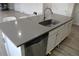 A kitchen island with a stainless steel sink, dishwasher, gray countertop and sleek, white cabinets offers modern functionality at 9694 Truckee St, Commerce City, CO 80022