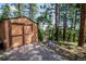 A well-maintained shed with double doors, nestled among tall trees and landscaping at 8624 S Doubleheader Ranch Rd, Morrison, CO 80465