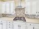 Gourmet kitchen boasts designer backsplash, stainless steel range hood, and white cabinets with dark hardware at 784 Sweet Pine Ct, Monument, CO 80132