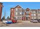Three-story apartment complex with gray siding, red brick, parking and nearby trees at 14251 E 1St Dr # 308, Aurora, CO 80011