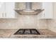 Close-up of cooktop featuring granite countertops, a tile backsplash, and stainless steel range hood at 3577 S Hillcrest Dr, Denver, CO 80237