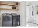 Modern laundry room with gray washer and dryer, open shelving, and a white tile floor at 1860 W Iris Cir, Littleton, CO 80120