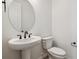 White powder room with a pedestal sink, round mirror, and elongated toilet at 574 Penn Rd, Elizabeth, CO 80107